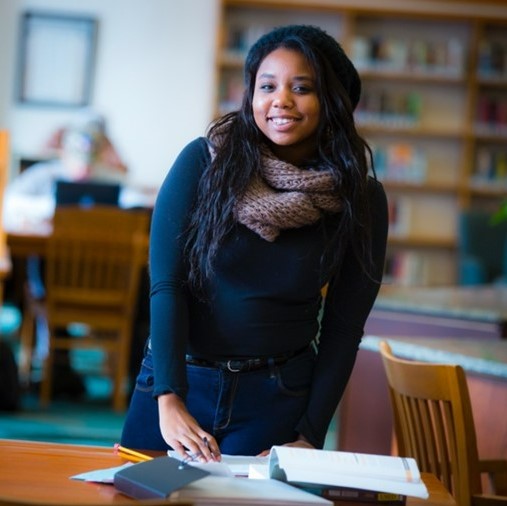 Image of a young woman smiling at a desk in a library