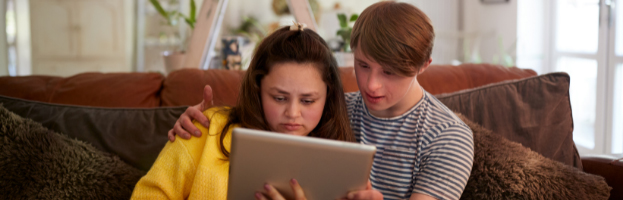 Two young adults sitting together on a couch using an ipad in the living room
