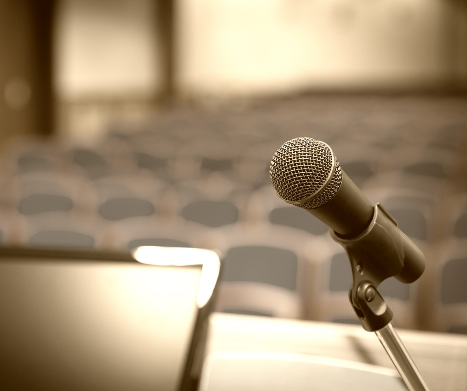 Close-up image of a microphone from the perspective of a presenter overlooking seats in an audience