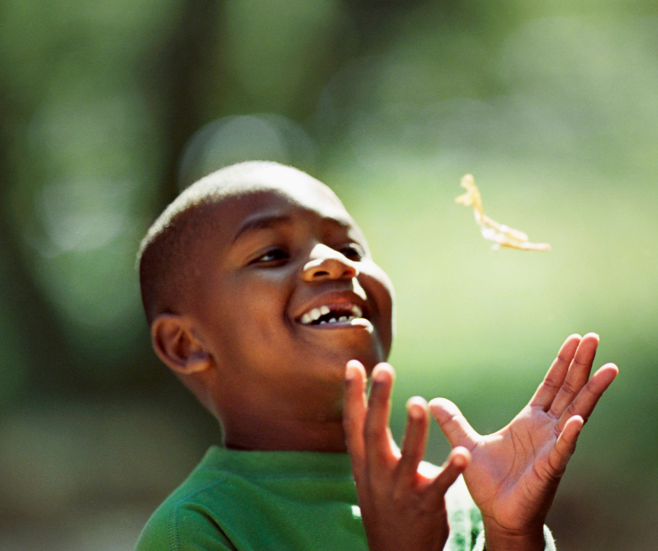 Image of a young boy smiling outside, about to catch something with his hands