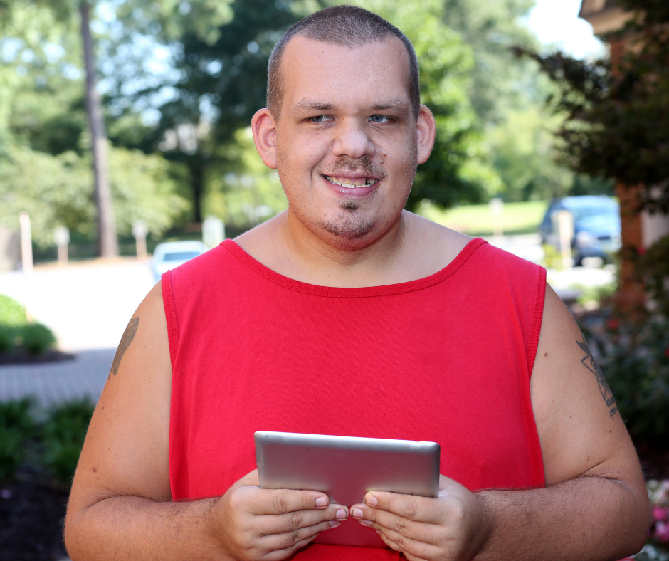 A man in a red shirt smiling outside while holding an iPad
